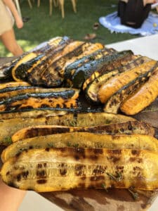 Grand plat de courgettes vertes et jaunes grillées, assaisonnées de thym et de sel, prêtes pour un repas en extérieur.