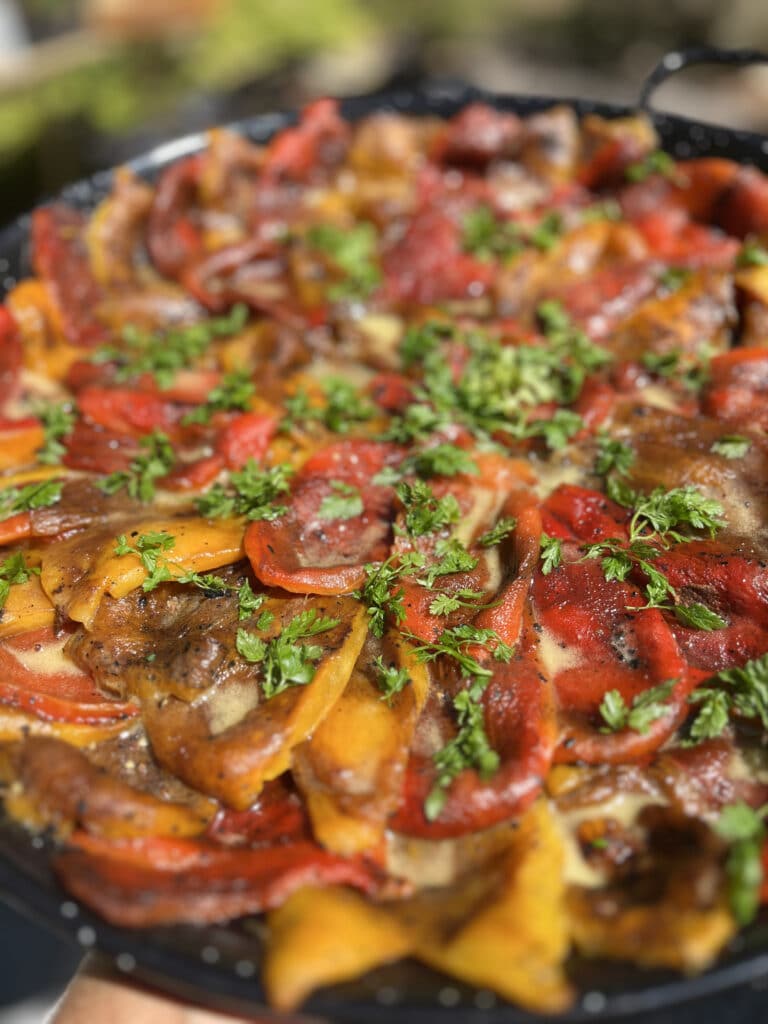 Plat de poivrons rôtis rouges et jaunes, parsemés de persil frais, dans une poêle noire. Texture brillante et légèrement carbonisée.