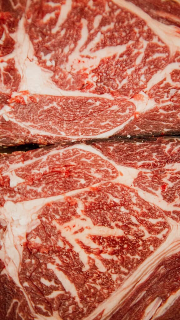 Tranches de bœuf cru premium, richement persillées de gras blanc crémeux. La marbrure dense et la couleur rouge vif indiquent une qualité supérieure.
